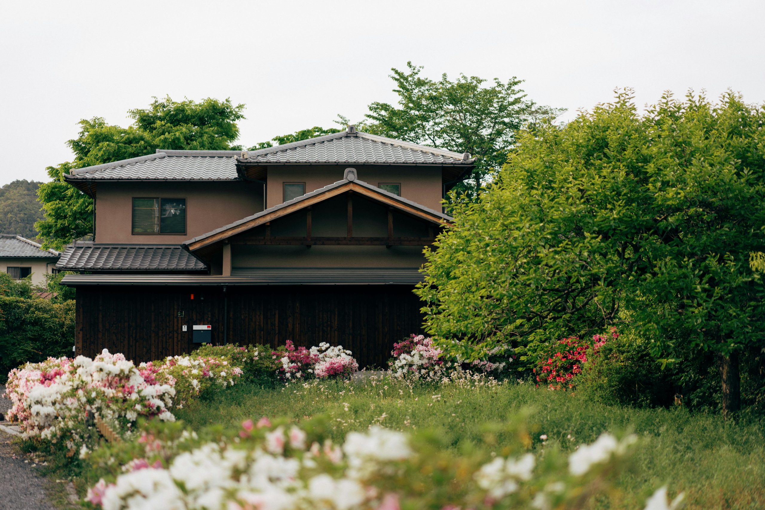 A serene image of a traditional Japanese house surrounded by lush greenery and blooming flowers.